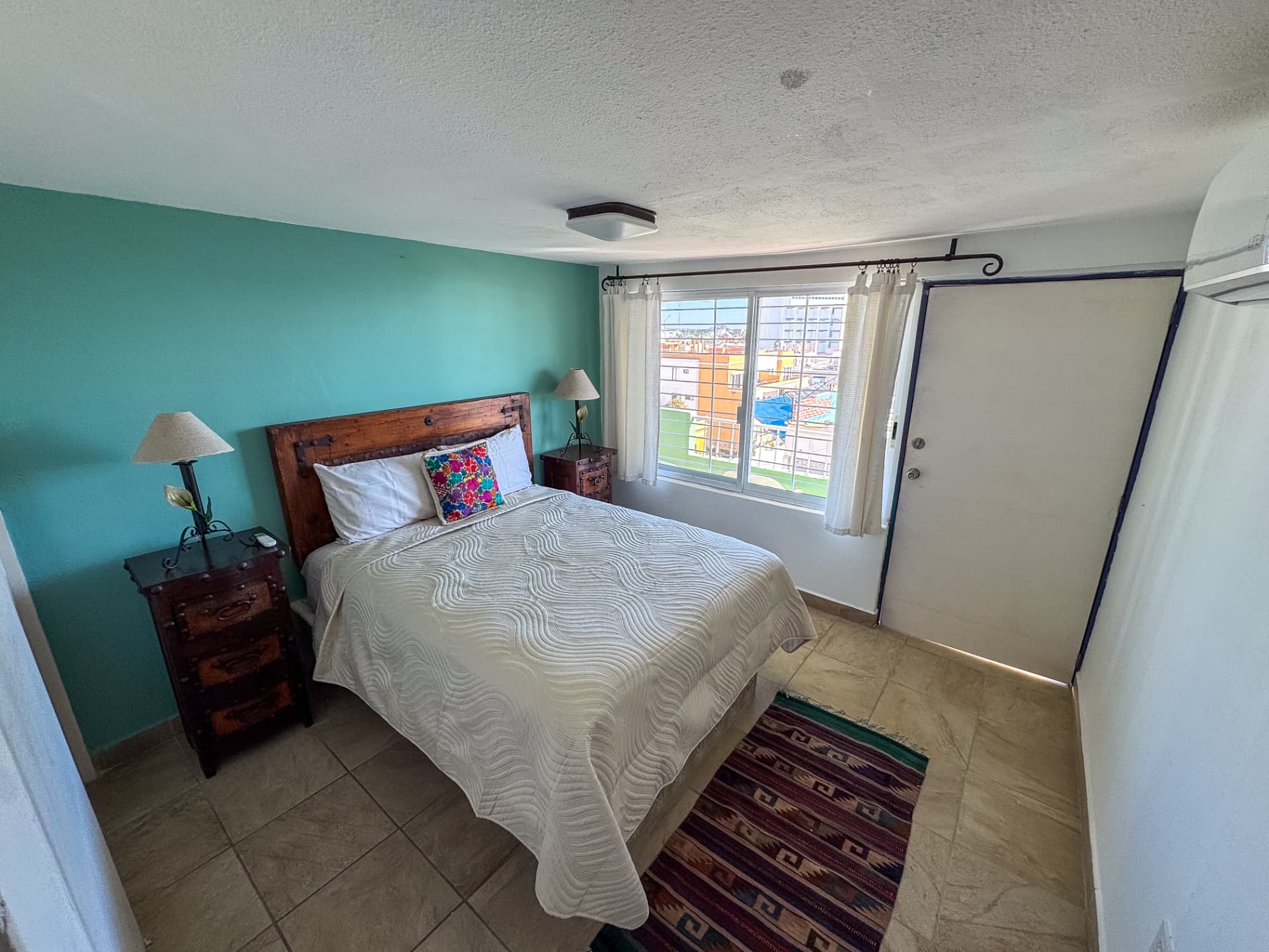 Habitación con muro verde jade, cama matrimonial y vista a la ciudad